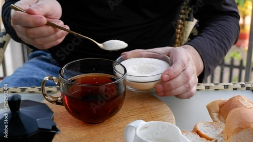 Male hands adding sugar into big cup of tea on table