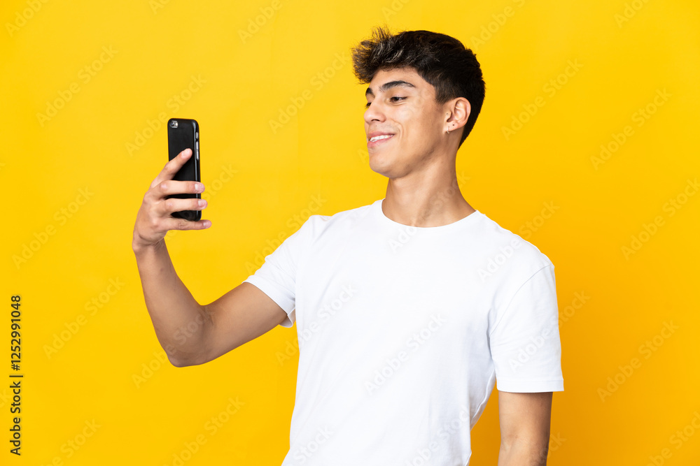 Young man over isolated yellow background making a selfie with mobile phone