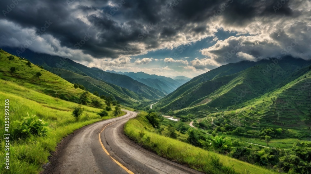 Fototapeta premium A winding mountain road through lush green valleys under a dramatic cloudy sky.