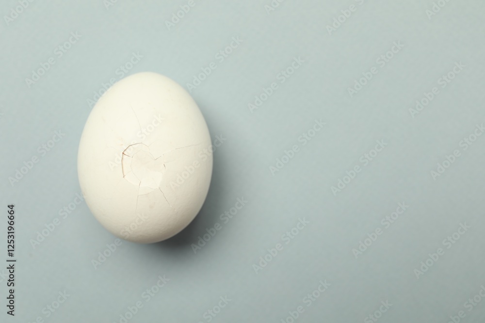 One egg with cracked shell on grey background, top view. Space for text One egg with cracked shell on grey background, top view. Space for text