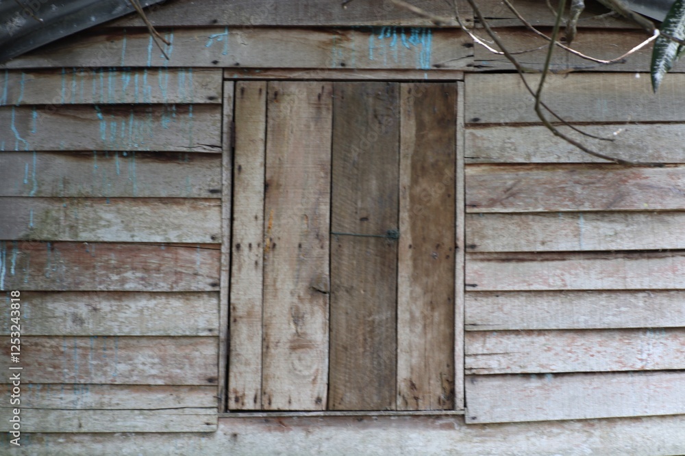 Weathered wooden shed facade with boarded window and hints of blue paint Weathered wooden shed facade with boarded window and hints of blue paint
