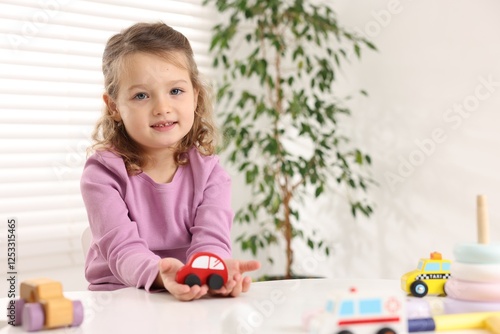 Little girl playing with toy cars at white table indoors, space for text