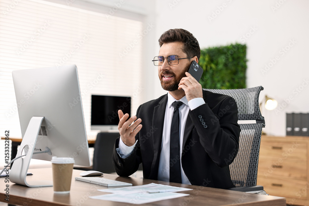 Man talking on smartphone while working at table in office Man talking on smartphone while working at table in office