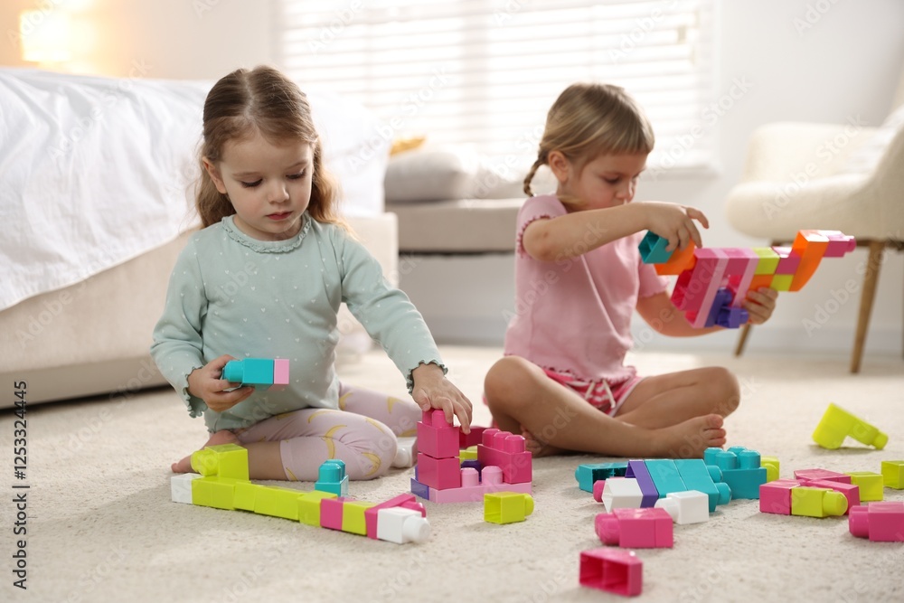 Cute little sisters playing with colorful building blocks on floor at home Cute little sisters playing with colorful building blocks on floor at home