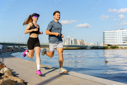 Two runners jog along a riverfront path in a modern city under clear blue skies photo