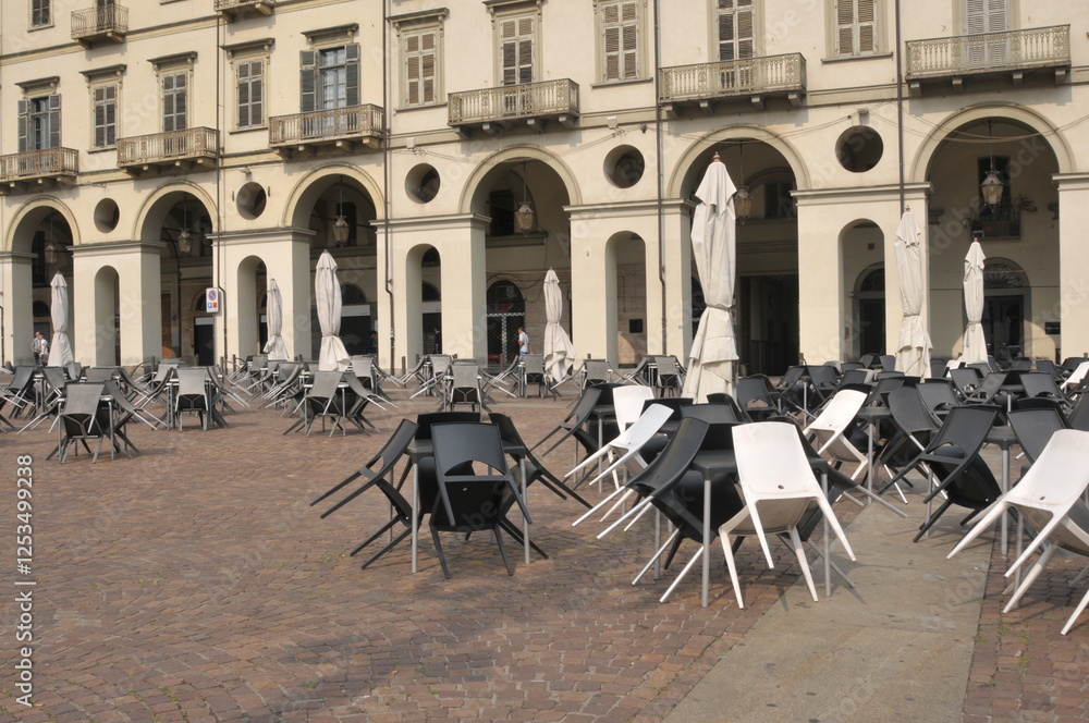 Naklejka premium ciudad antigua de Europa ,Venecia, lugar para comer cerrado con sillas y sombrillas típicas en horario que no hay gente circulando, edificio con arcadas típicas e época , balcones, ventanas , galería 