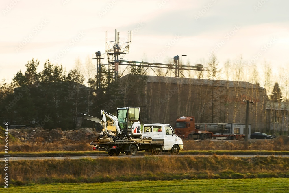 Fototapeta premium Yellow truck transporting excavator on construction site road