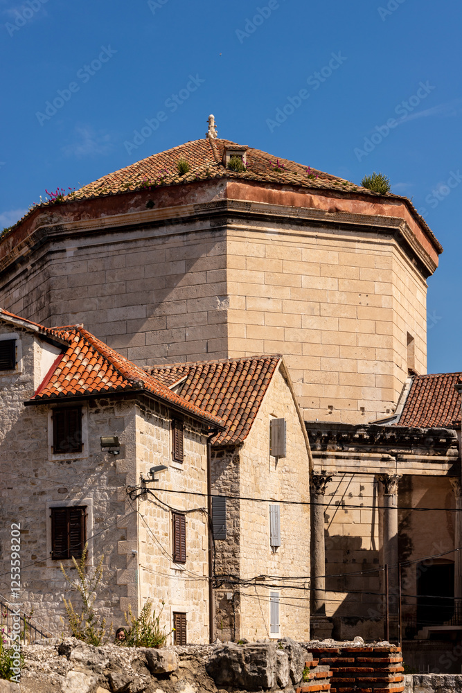 Fototapeta premium Historic Stone Buildings with Tiled Roofs in Croatia. A scenic view of old stone buildings with terracotta-tiled roofs in Croatia. Historic architecture with weathered walls and a blue sky in the back