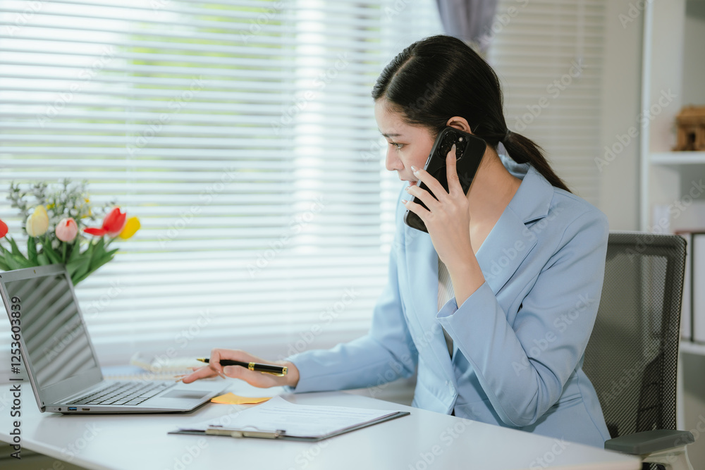 Beautiful Asian businesswoman sitting at desk in office with documents and laptop computer.