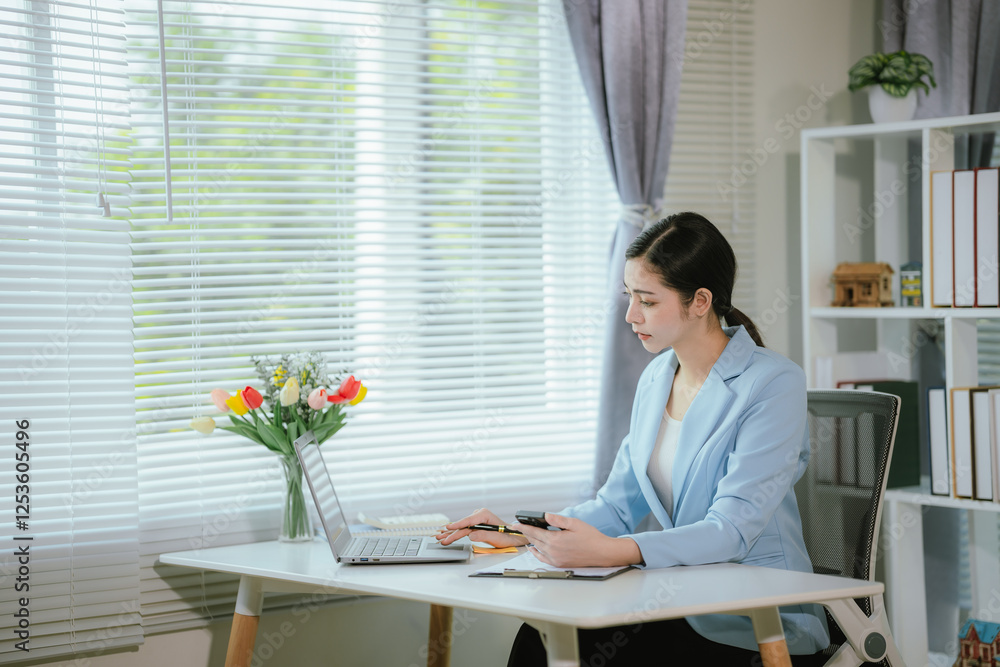 Asian businesswoman sitting at desk in office with documents and laptop computer. Asian businesswoman sitting at desk in office with documents and laptop computer.