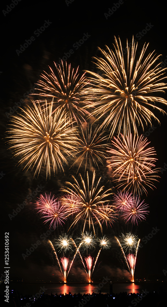 Dazzling Fireworks Display: Night Sky Spectacle of Gold, Pink, and Red Bursts over Water Dazzling Fireworks Display: Night Sky Spectacle of Gold, Pink, and Red Bursts over Water