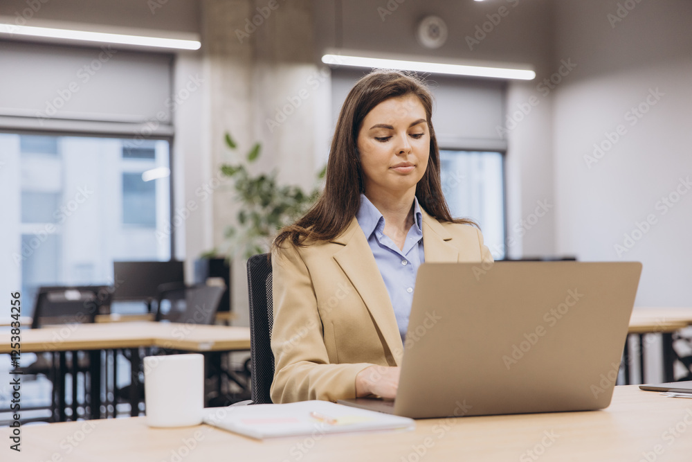 Focused businesswoman sitting at a desk, working intently on a laptop in a bright, modern office filled with natural light Focused businesswoman sitting at a desk, working intently on a laptop in a bright, modern office filled with natural light