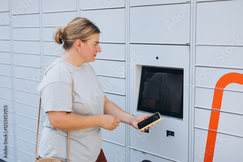 Parcel delivery machine. Mail delivery and post service concept. Happy smiling woman with phone at outdoor automated parcel machine. Electronic locker for storing parcels. photo