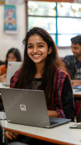An Indian student sitting in the classroom and smiling while using their laptop
