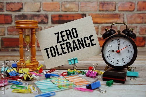 Zero Tolerance text on paper card with alarm clock and stationary on wooden background photo