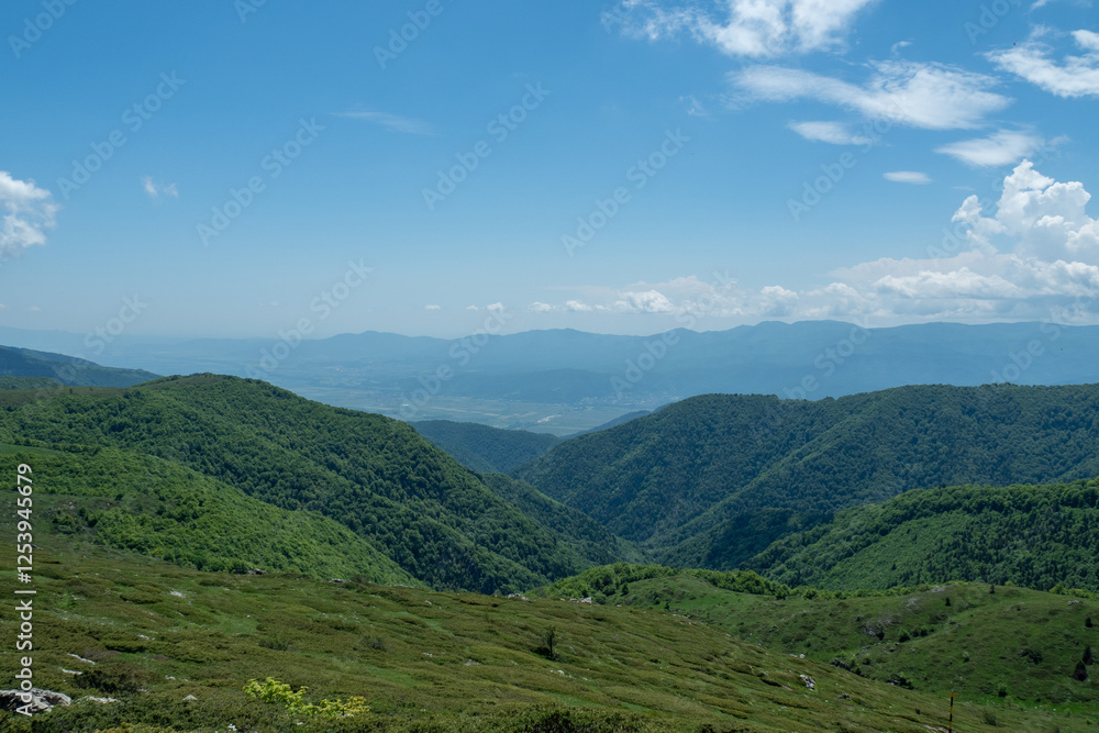 Fototapeta premium Scenic mountain landscape with green hills under a blue sky, showcasing nature's beauty and tranquility. Ideal for themes of outdoor exploration and vibrant springtime scenery - Bulgaria, Europe