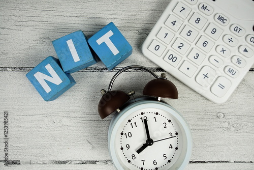 NIT (Negative Income Tax) text with alarm clock and calculator on wooden background photo