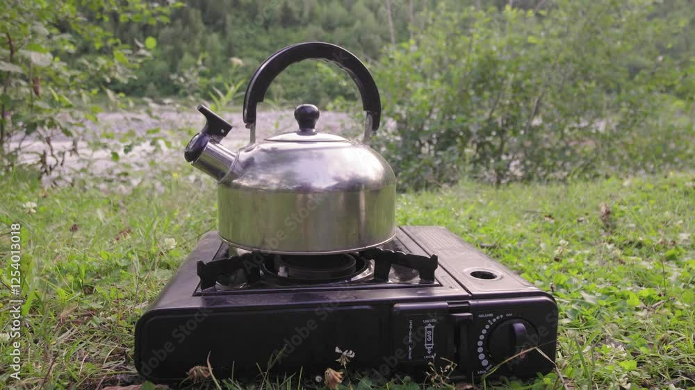 Stainless steel kettle heating over portable gas stove amid lush wilderness landscape, showcasing serene outdoor cooking moment during camping adventure and peaceful nature retreat Stainless steel kettle heating over portable gas stove amid lush wilderness landscape, showcasing serene outdoor cooking moment during camping adventure and peaceful nature retreat