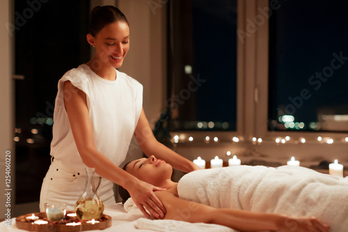 Professional masseuse performing full body massage to young woman client in wellness spa center in tranquil calm candlelit atmosphere