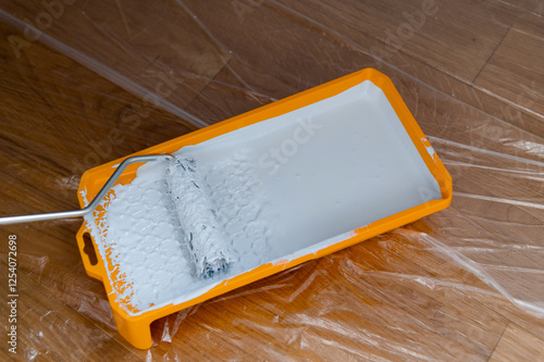 Painting a room with white paint using a roller and tray on a wooden floor photo