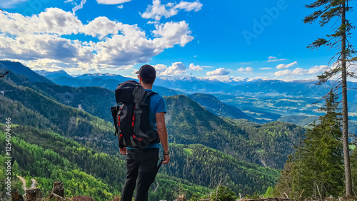 Man on alpine pasture with view of distant High Tauern mountain range from the Gailtal Alps. Scenery captures vastness of the Austrian landscape under a bright, partly cloudy sky. Remote Austria Alps photo