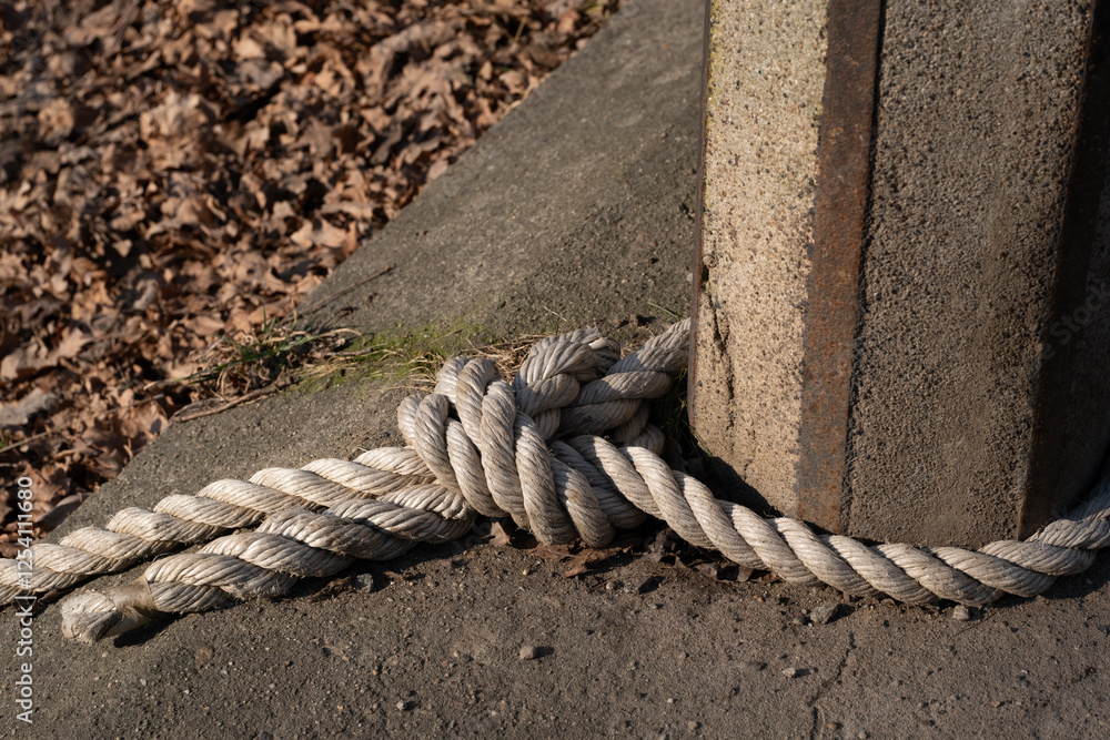 Fototapeta premium A thick, white rope tied in a strong knot around a weathered concrete post. The fibers of the rope appear slightly frayed, adding texture and character to the image. 