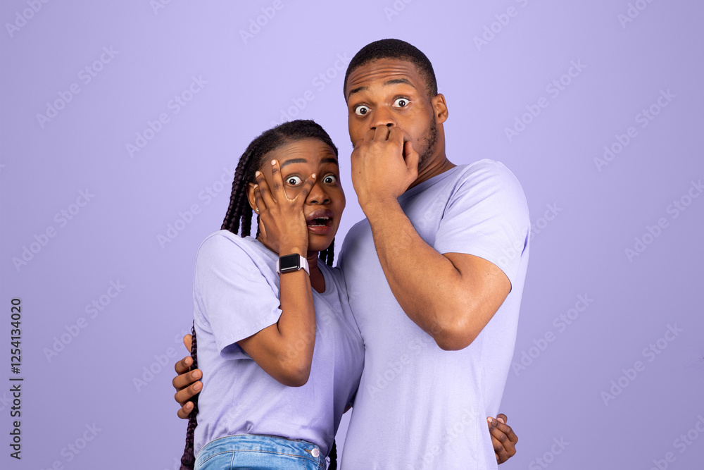 Obraz premium Omg. Portrait of scared African American couple covering mouth and eyes, woman jumping on man, looking at camera standing isolated on purple violet studio background. Human emotions, facial expression
