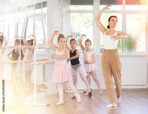 Adult female teacher shows ballet choreography to group of girl dancers in studio photo