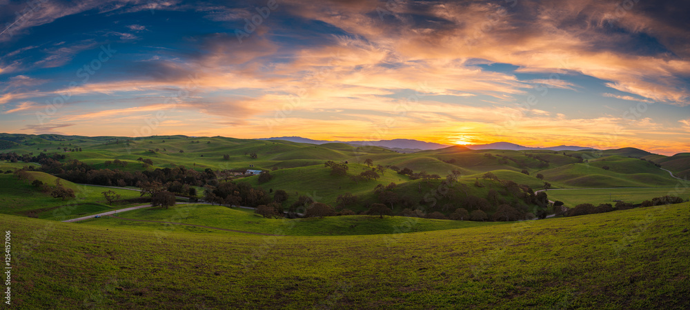 Fototapeta premium Sunset over the Mountain Landscape with Green Meadows and Cloudy Skies