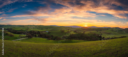 Sunset over the Mountain Landscape with Green Meadows and Cloudy Skies