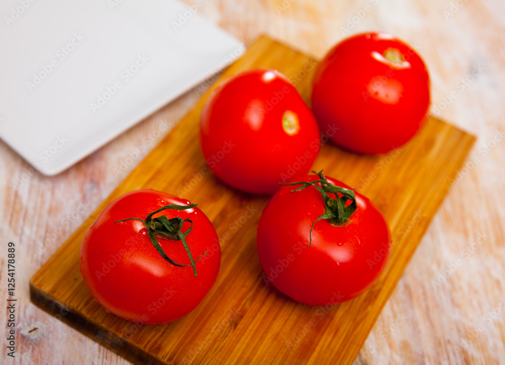 Ripe juicy tomatoes on cutting board on kitchen table. Preparing food concept. Ripe juicy tomatoes on cutting board on kitchen table. Preparing food concept.