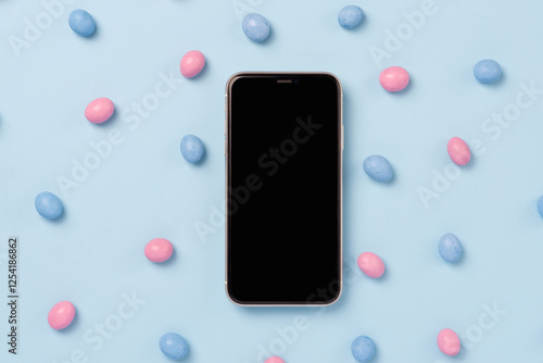 Top view of mobile phone with black screen and easter dragee on a blue background. Mockup template for Easter photo