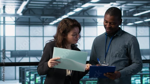 IT professionals in data center reviewing reports and files, crosschecking network performance metrics and security logs. Server room workers doing troubleshooting to prevent downtime, camera A photo