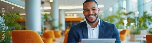 A smiling man in a suit holds a tablet in a modern, bright space filled with plants, reflecting a professional yet relaxed atmosphere.