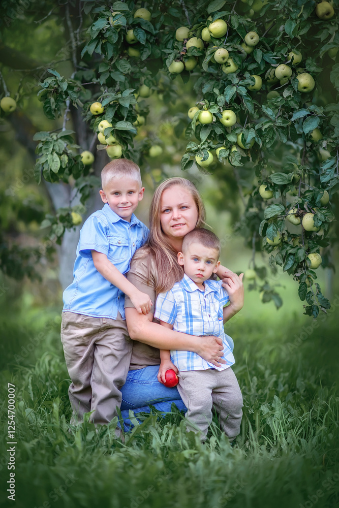 Portrait of a mother and two sons. Mom tenderly hugs her sons. Mom and sons are sitting under an apple tree. Family on a summer day for a walk in the garden. Mom and sons are harvesting. Happy family Portrait of a mother and two sons. Mom tenderly hugs her sons. Mom and sons are sitting under an apple tree. Family on a summer day for a walk in the garden. Mom and sons are harvesting. Happy family