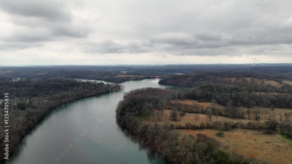 Drone view of a tranquil river surrounded by autumnal fields under gray cloudy sky Drone view of a tranquil river surrounded by autumnal fields under gray cloudy sky