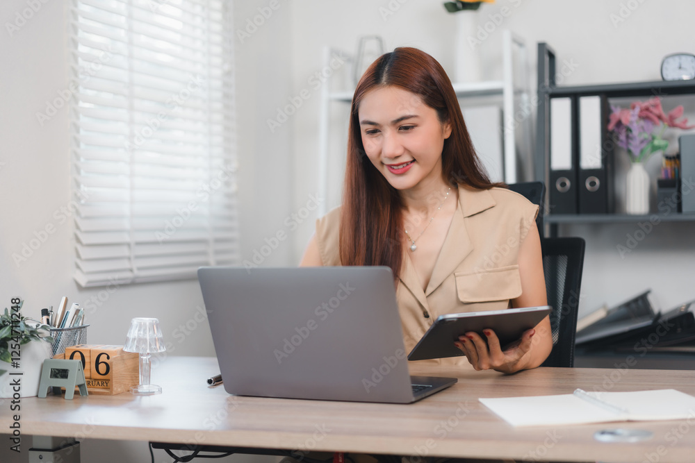 Woman working at desk with laptop and tablet in bright office setting. Woman working at desk with laptop and tablet in bright office setting.