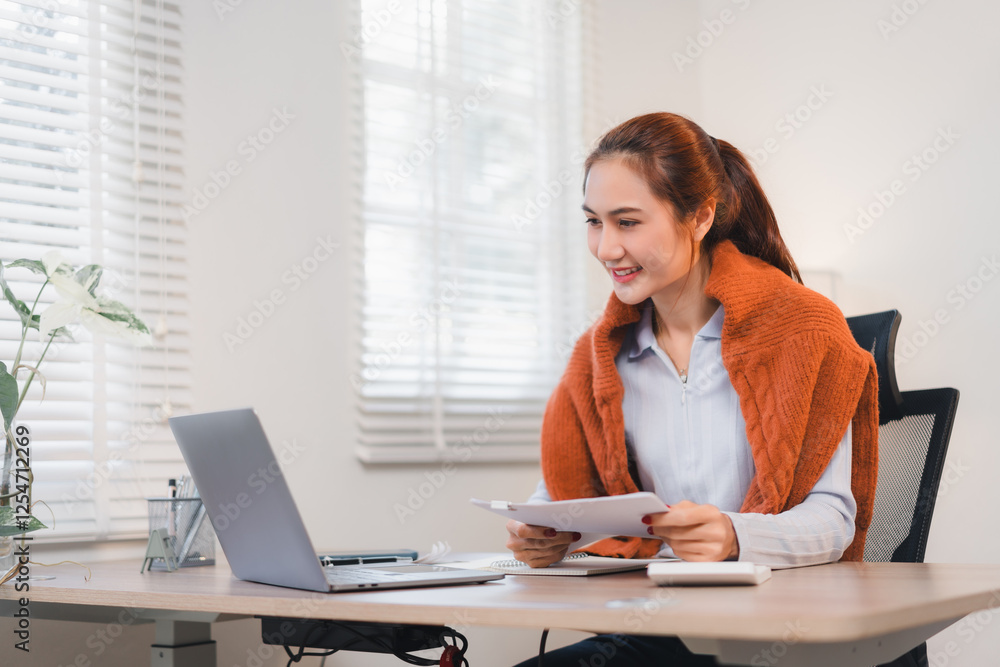 Woman working at desk with laptop, holding documents and smiling in bright office. Woman working at desk with laptop, holding documents and smiling in bright office.