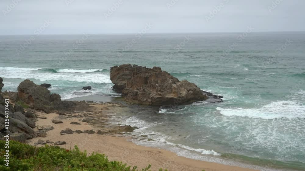 Slow motion rolling waves with a big beach boulder on a cloudy day Slow motion rolling waves with a big beach boulder on a cloudy day