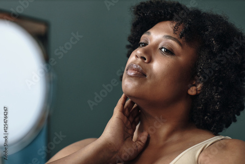 Young African American woman enjoying moment of calm while gently touching neck. Lightly smiling and gazing into distance photo