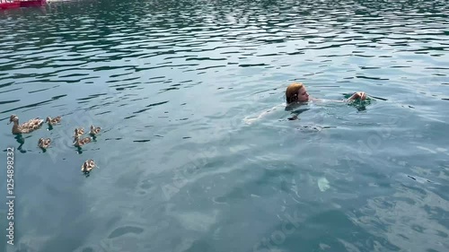 Girl is swimming in the pond among small ducklings