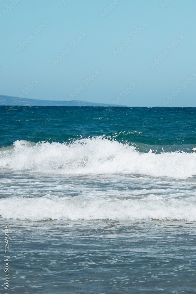 Waves gently lap against the shore on a sunny day at a tranquil beach. vertical Waves gently lap against the shore on a sunny day at a tranquil beach. vertical