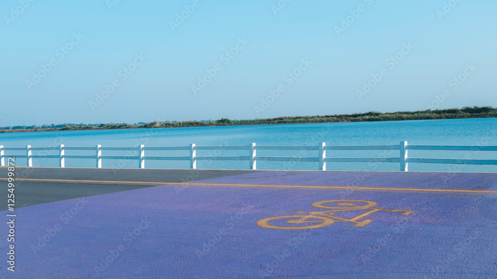Blue and purple parking lot with a bike symbol on the ground. The parking lot is next to a body of water