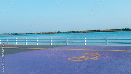 Obraz na płótnie Blue and purple parking lot with a bike symbol on the ground. The parking lot is next to a body of water w salonie