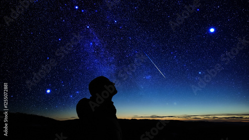 Silhouette of a man observing Milky Way stars, planets and other celestial objects from a dark countryside location.