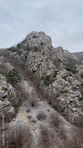 A rugged mountain landscape in Senjska Draga, featuring rocky cliffs, sparse vegetation, and a cloudy sky, captured in HDR. The scene is serene and showcases natural beauty. photo