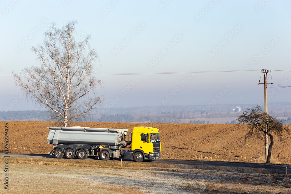 A large truck drives along a road in the countryside on a cold winter morning.