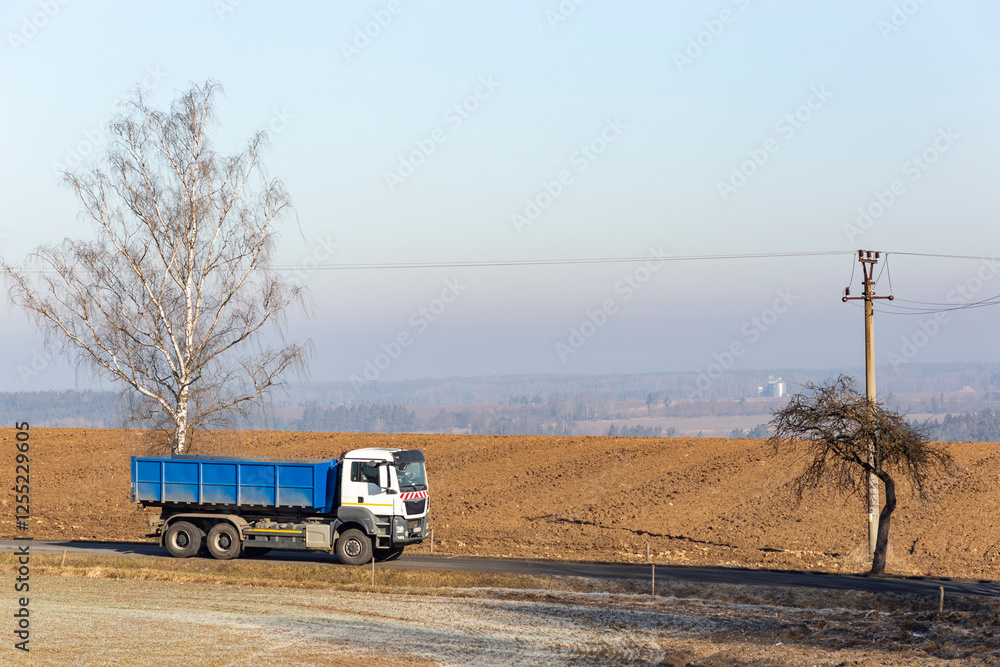 A large truck drives along a road in the countryside on a cold winter morning.