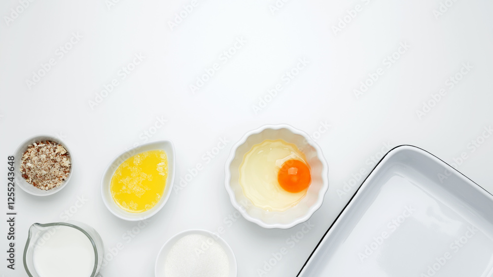 Flat lay composition for cooking preparation. Empty white baking dish with ingredients for baking, including egg, milk, butter, sugar, nuts