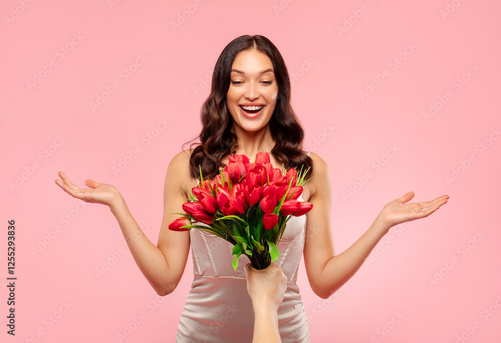 Excited young woman with open mouth rejoicing to gift bouquet of red tulips, receiving gift for women's day, spring holiday, isolated on pink background Excited young woman with open mouth rejoicing to gift bouquet of red tulips, receiving gift for women's day, spring holiday, isolated on pink background